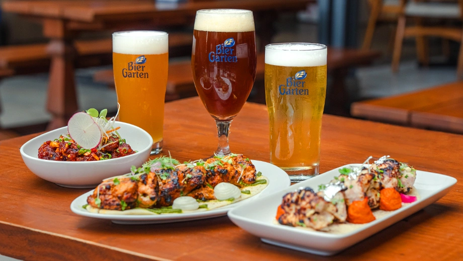 Fresh craft beer glasses paired with tandoori starters and appetizers on a wooden table at Biergarten, one of the top restaurants in Bellandur.