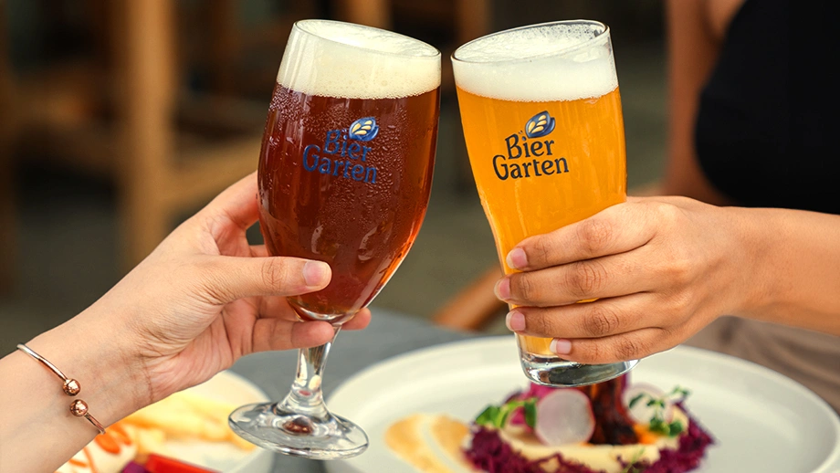 Two people toasting with fresh craft beer glasses over a meal at Biergarten, one of the best breweries in Bangalore.